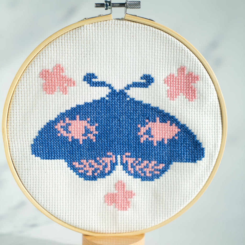 Block blue moth with pink detailing on cross stitch piece